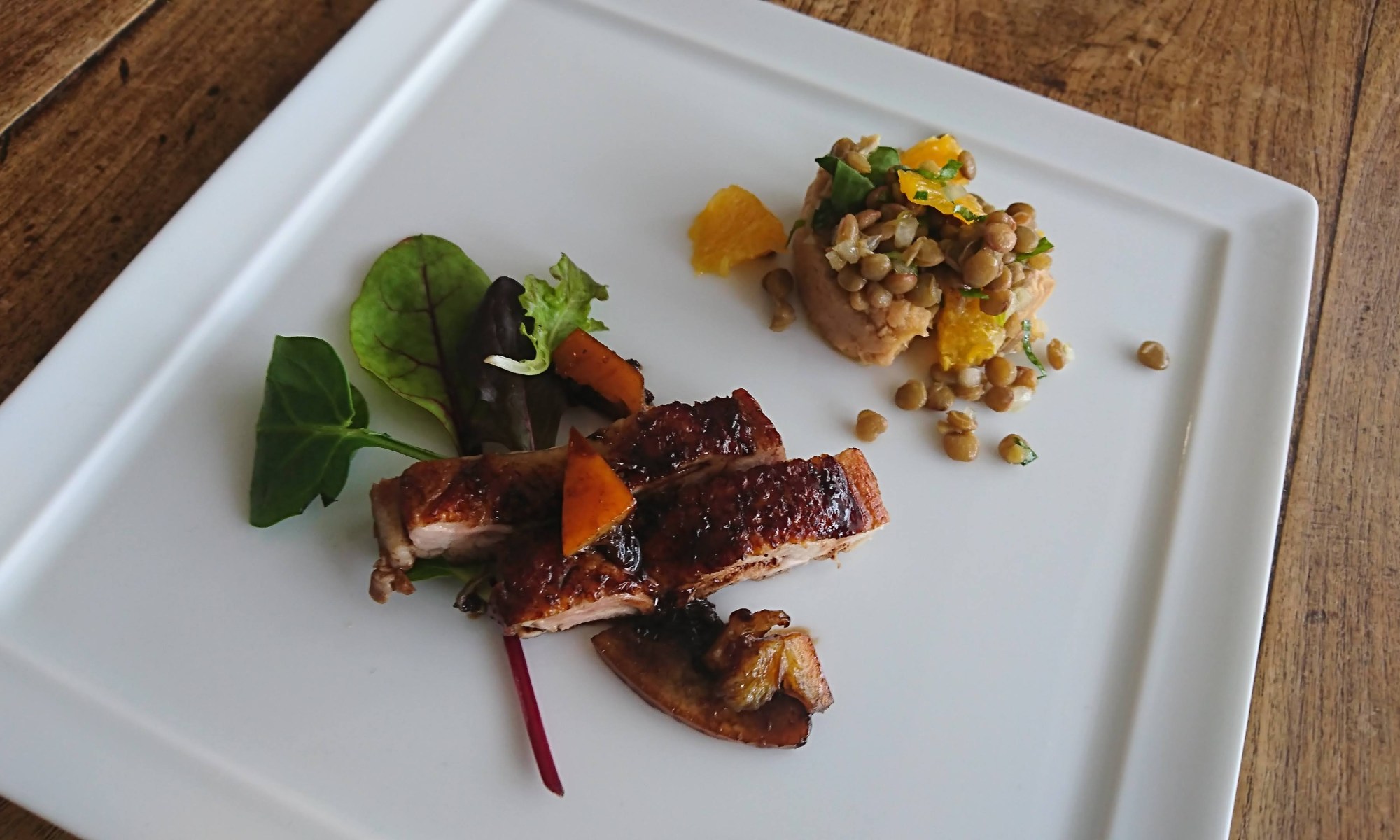 四角い白皿にチキングリルとレンズ豆＆オレンジのサラダが盛り付けられています