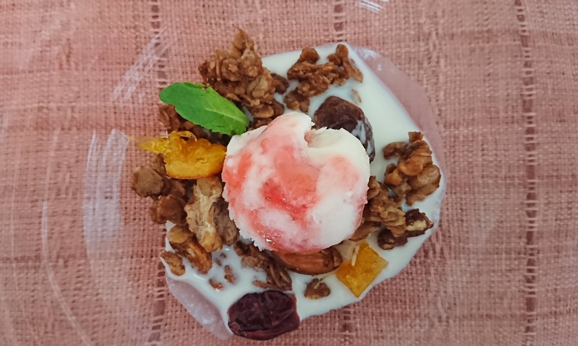 ガラスの器にグラノーラとマーブル状の苺アイスと甘酒が盛り付けられています