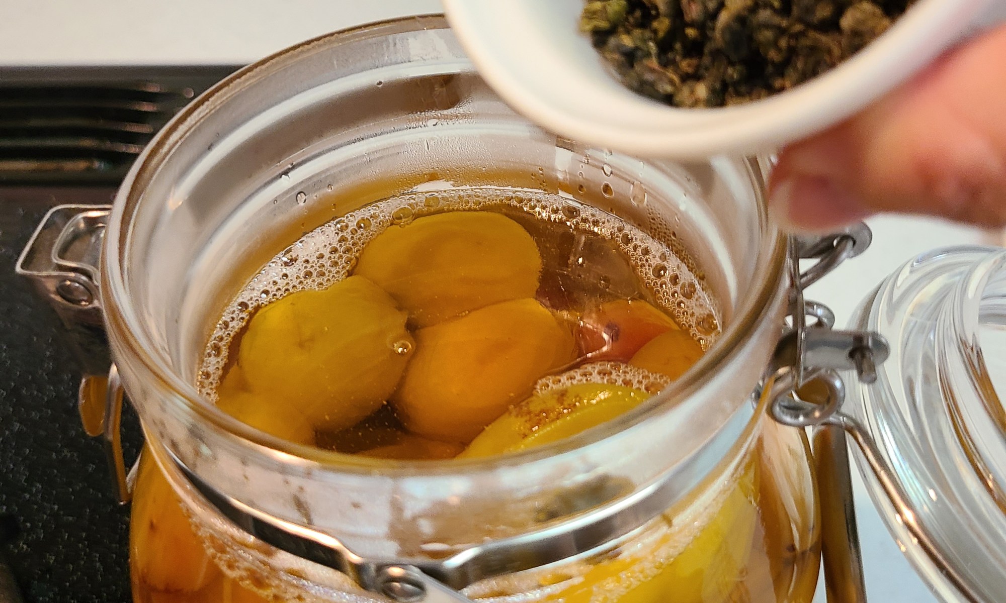 煮た梅が入った瓶に茶葉を加えている