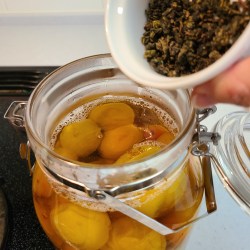 煮た梅が入った瓶に茶葉を加えている