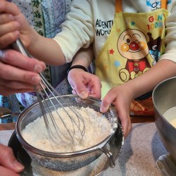 男の子が泡立て器で粉を振るっている