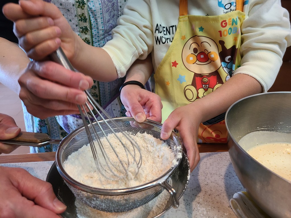 男の子が泡立て器で粉を振るっている