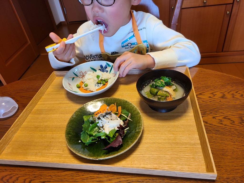 お盆の並んだお料理を男の子が食べています